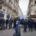 Uma mulher vista passando perto de um esquadrão policial durante o comício de 13 de outubro de 2023 em Paris [Telmo Pinto/SOPA Images/LightRocket via Getty Images]