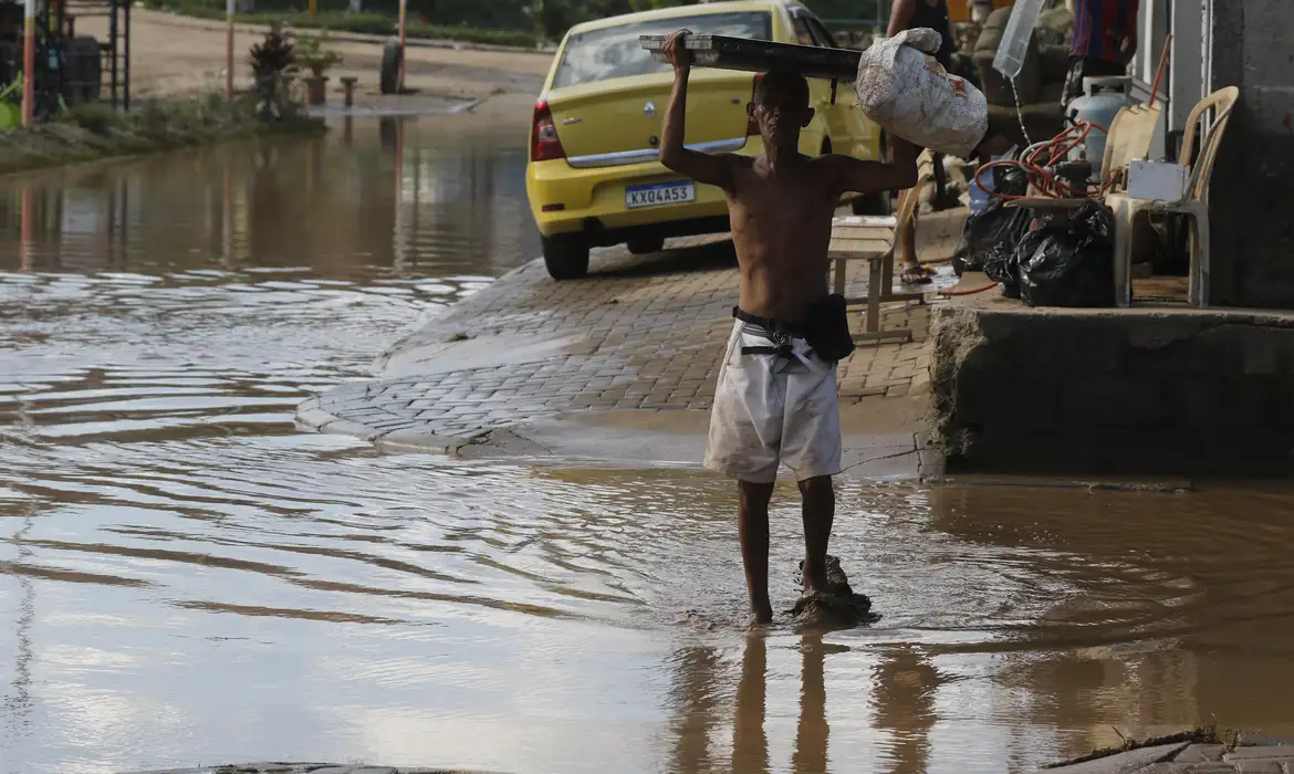 Chuva forte que atingiu a Baixada Fluminense no último fim de semana deixou milhares de pessoas desalojadas e causou prejuízos materiais. Para o professor de Recursos Hídricos da Coppe/UFRJ, Paulo Canedo, a principal causa das enchentes foi a falta de manutenção no sistema de drenagem da região. O que você precisa saber: A falta de manutenção no sistema de drenagem é a principal causa das enchentes na Baixada Fluminense. O Projeto Iguaçu, que objetivava promover a recuperação ambiental das bacias da Baixada e da zona oeste do Rio de Janeiro, poderia ter contribuído para reduzir os impactos das enchentes. A paralisação do Projeto Iguaçu pela crise econômica foi um fator que contribuiu para o aumento das enchentes. Corpo do texto: O professor Canedo explica que as comportas do sistema de drenagem da Baixada não estão funcionando e, como não tem tido manutenção nos últimos dez anos, a infraestrutura implantada ficou inoperante. "Com a chuva forte que caiu no último final de semana, com grande volume precipitado, a estrutura que foi criada para proteger a região da Baixada, não funcionando, não deu conta do recado e não consegue botar para fora (a água acumulada)", disse. A isso se somam o problema da poluição, o acúmulo de lixo e o assoreamento de rios. "O mau trato que a população dá ao sistema é grande. E isso contribui para que fique ruim. Porque entra lixo e isso causa problema", admitiu. Destacou, porém, que, independente disso, se o sistema estivesse operando, o problema seria "muitíssimo" menor. "Você tem a conjugação de três coisas importantes: a chuva com volume muito grande; o sistema que foi implementado para escoar não está funcionando, por falta de manutenção nos últimos dez ou 12 anos; e a população não tem feito também sua contribuição de não jogar lixo nos rios, nas ruas, para não entupir os bueiros. A conjugação desses três efeitos gera esse caos que gerou". O professor Canedo também avalia que o Projeto Iguaçu, que objetivava promover a recuperação ambiental das bacias da Baixada e da zona oeste do Rio de Janeiro, poderia ter contribuído para reduzir os impactos das enchentes. "O projeto foi implementado com razoável força até 2012 e, depois, tivemos um azar, porque o Brasil ficou em uma situação ruim com a crise econômica, tivemos uma crise econômica no estado do Rio de Janeiro e não nos livramos dessa crise", afirmou. Segundo o professor, a paralisação do Projeto Iguaçu "pegou a Baixada de calça curta, com essa chuva". "O projeto continua fazendo parte do PAC. Analisou que por maiores que sejam as dificuldades que o estado e o país vivenciem, não podem abandonar as conquistas feitas, referindo-se ao Iguaçu. "Se o estado fez um investimento em defesa contra inundação, ele pode parar de ampliar essa defesa, mas não pode abandonar o que já foi feito, porque, senão, você perde o ganho feito", concluiu.