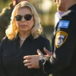 Sara Netanyahu conversa com um membro da polícia israelense enquanto visita um memorial com fotos de pessoas mortas durante o ataque do Hamas ao festival Super Nova, em 30 de novembro de 2023, em Re'im, Israel [Alexi J. Rosenfeld/Getty Images]