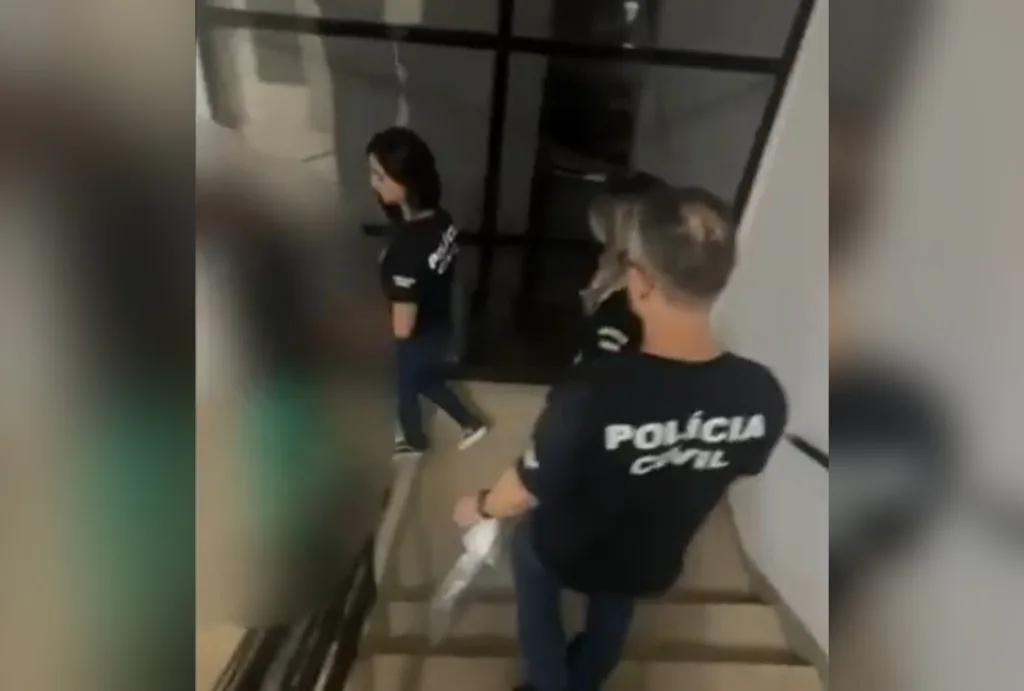 Acusado, com a imagem borrada, descem as escadas da delegacia acompanhados por policiais