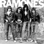 Integrantes da banda punk, Ramones, em pé, em frente a muro de tijolos Foto em preto e branco.