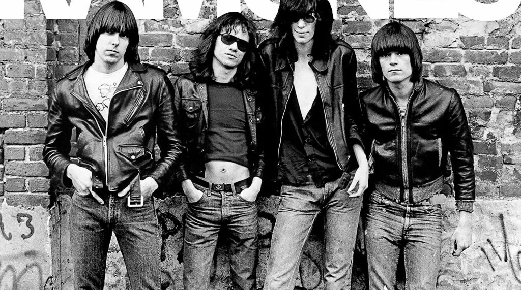 Integrantes da banda punk, Ramones, em pé, em frente a muro de tijolos Foto em preto e branco.