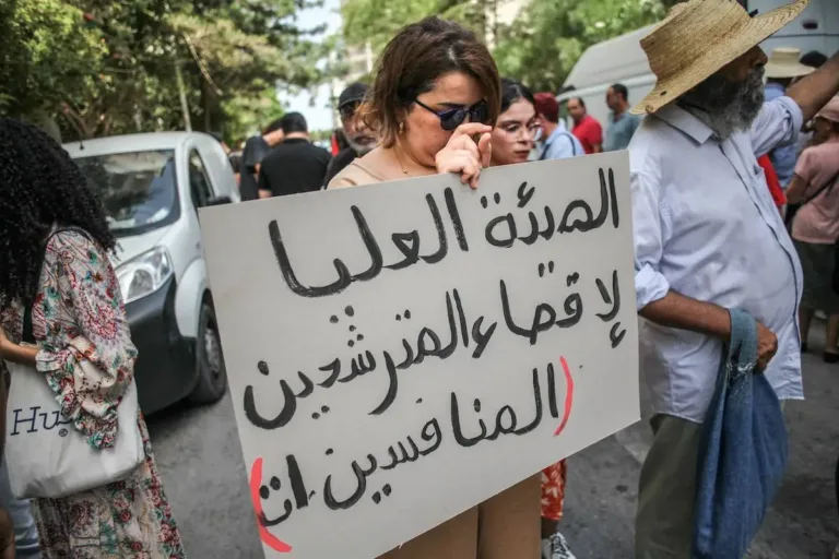 Manifestante segura um cartaz que diz em árabe, ''a Alta Autoridade elimina os candidatos concorrentes'', durante uma manifestação encenada por ativistas de direitos humanos, organizações de direitos das mulheres e grupos da sociedade civil do lado de fora da sede da Alta Autoridade Independente para as Eleições (em francês: ISIE) em Túnis, Tunísia, em 2 de setembro de 2024, para protestar contra a decisão do ISIE de excluir três candidatos às eleições presidenciais e o anúncio da lista final de candidatos oficialmente concorrendo às eleições presidenciais da Tunísia. [ Chedly Ben Ibrahim/NurPhoto via Getty Images]